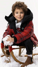 Две момчета в зимни якета Gulliver играят в сняг върху дървена шейна; едното носи яке с надпис ‘Never Look Back’